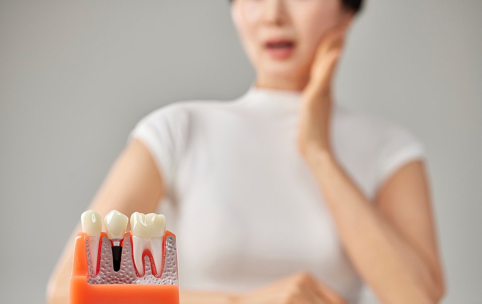 치아 단면 모형 뒤로 볼을 짚고 통증을 호소하는 모습
